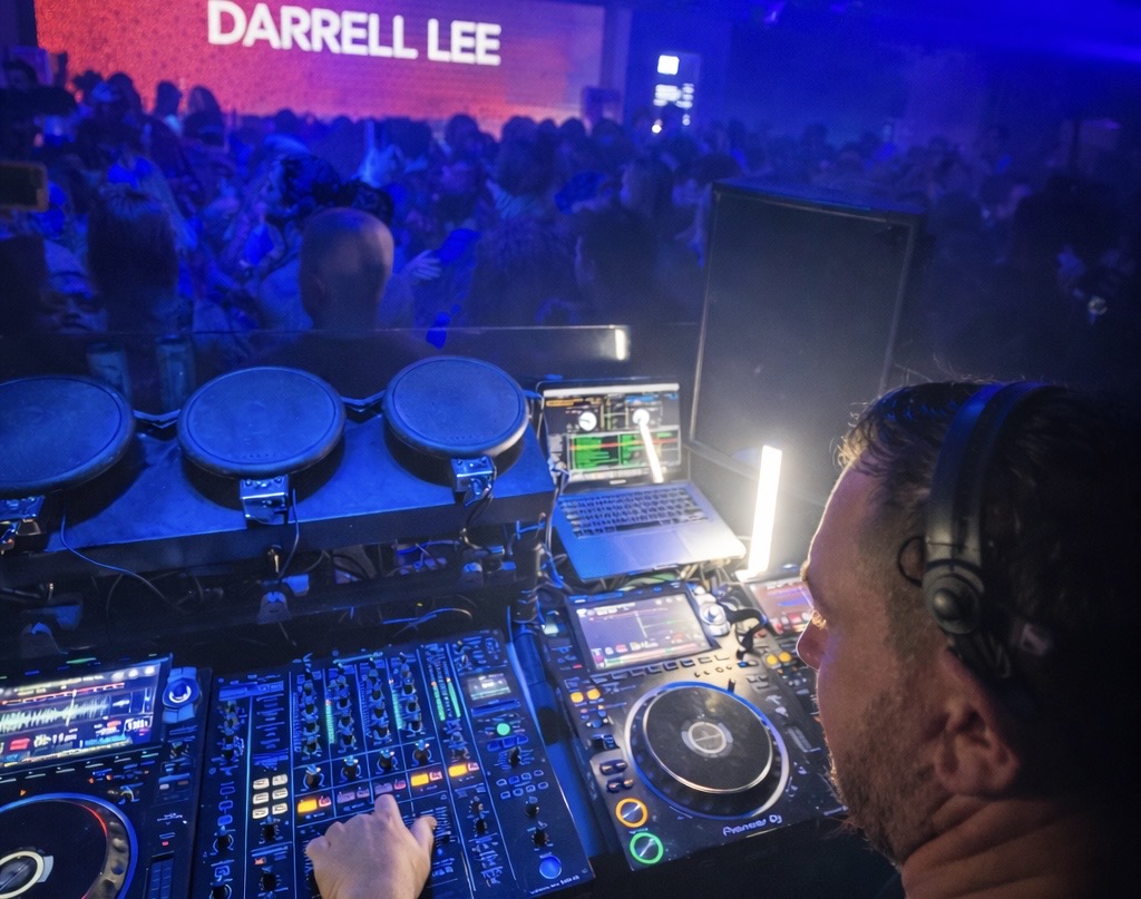 Darrell Lee playing a packed club night, his name lit up on the screen behind the decks